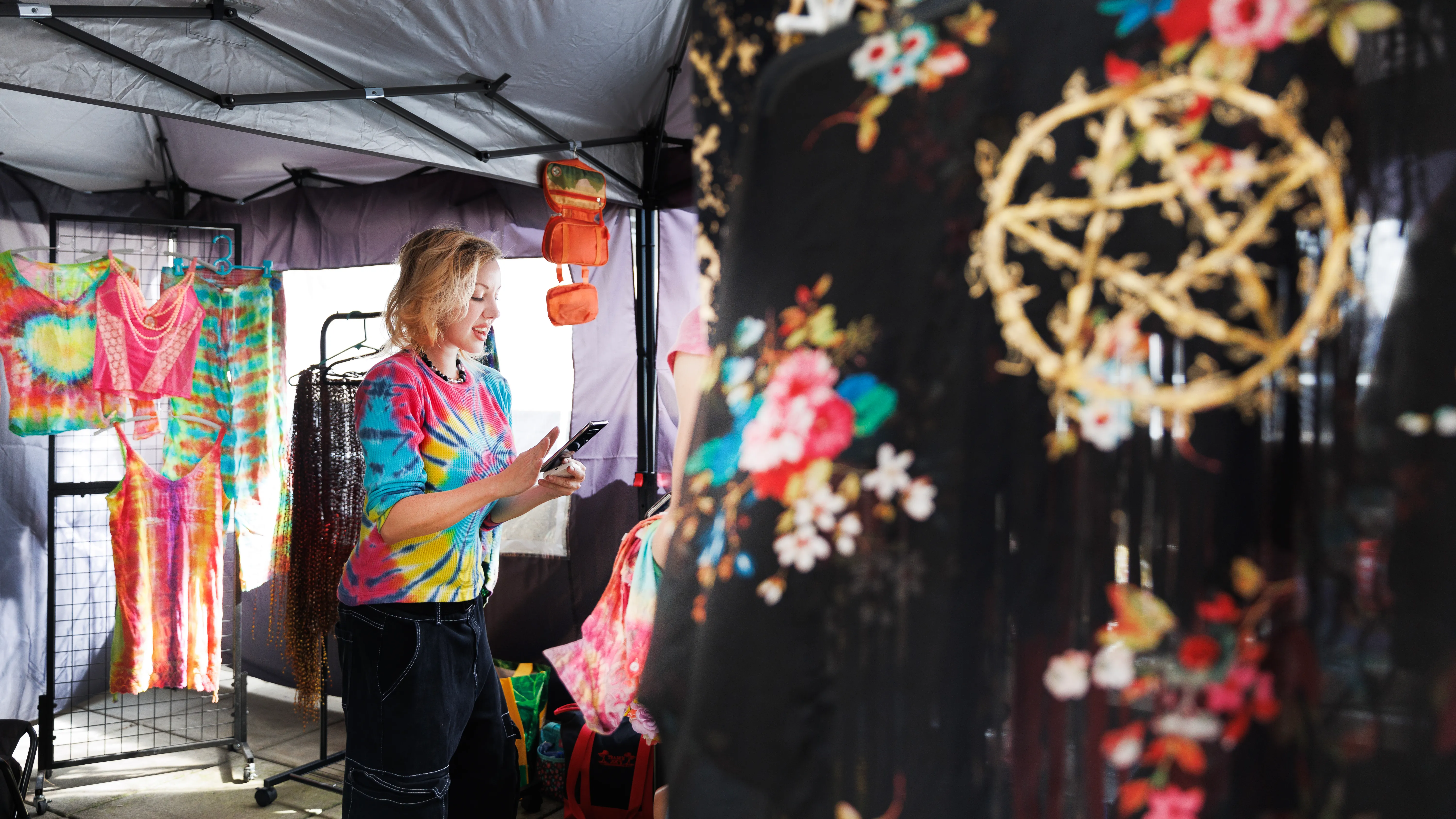 A local artist in a tie-dyed shirt with a curtain in the foreground of her vendor booth adorned with a flaming pentagram.