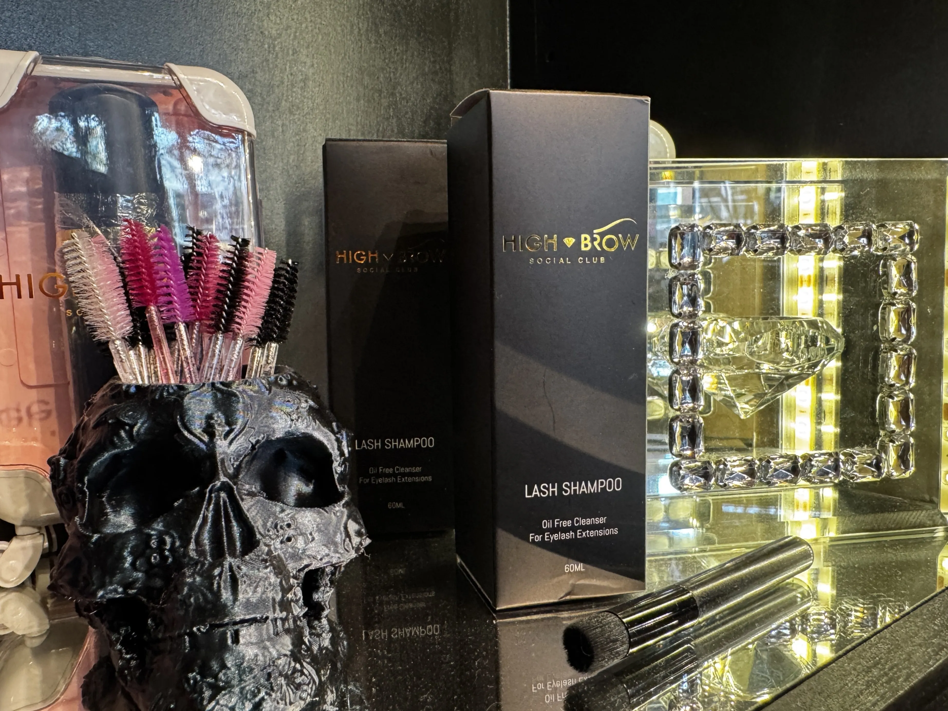 A skull shaped cup full of mascara brushes next to exclusive High Brow Social Club cosmetics